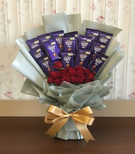 Luxury bouquet featuring Cadbury Dairy Milk chocolates arranged with fresh red roses, wrapped in light Korean-style paper and tied with a gold ribbon